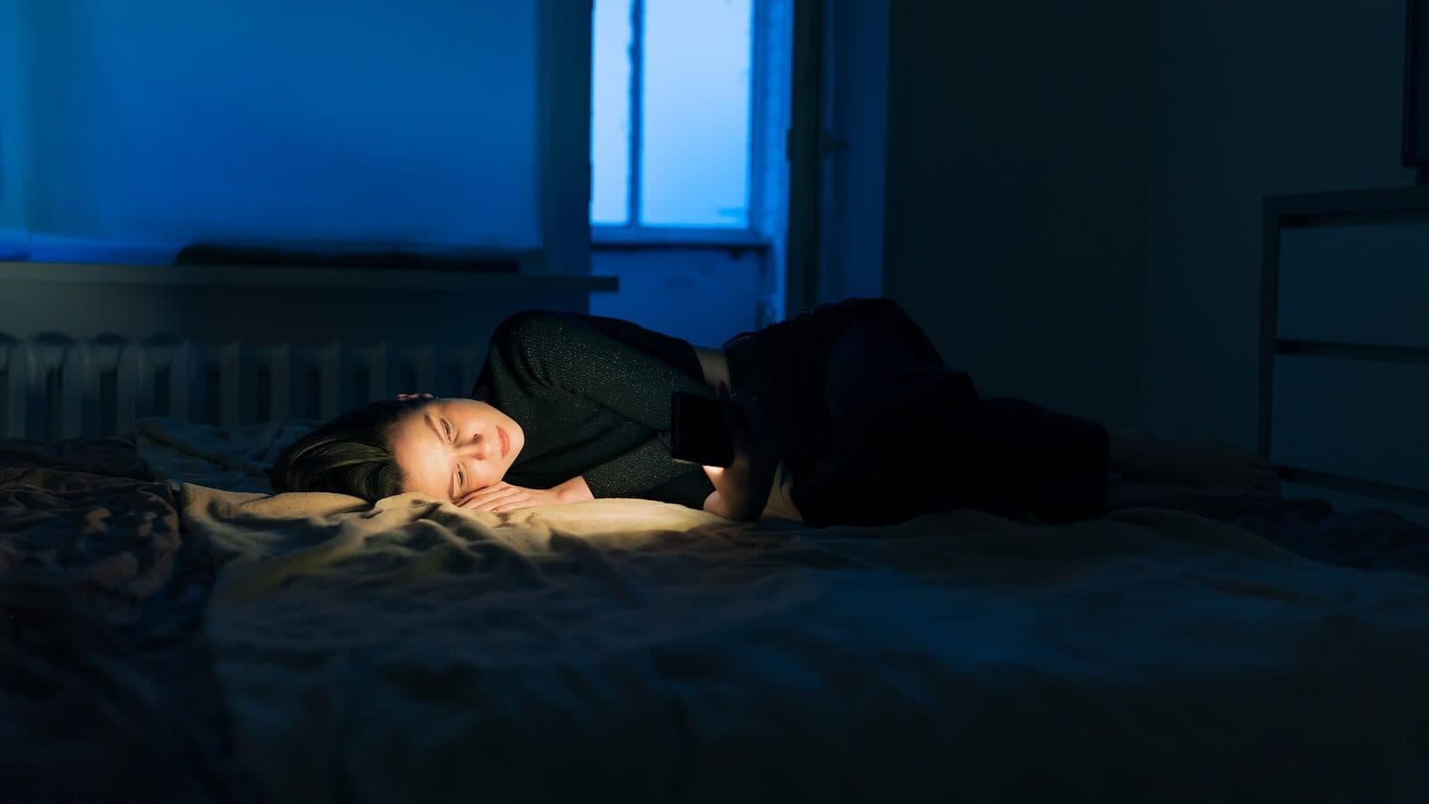 Persoon die ’s nachts wakker ligt met telefoonlicht in bed