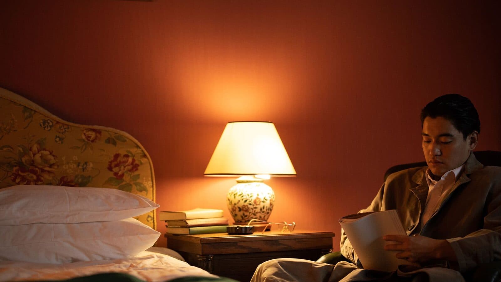 Man leest in een stoel bij het licht van een lamp naast het bed