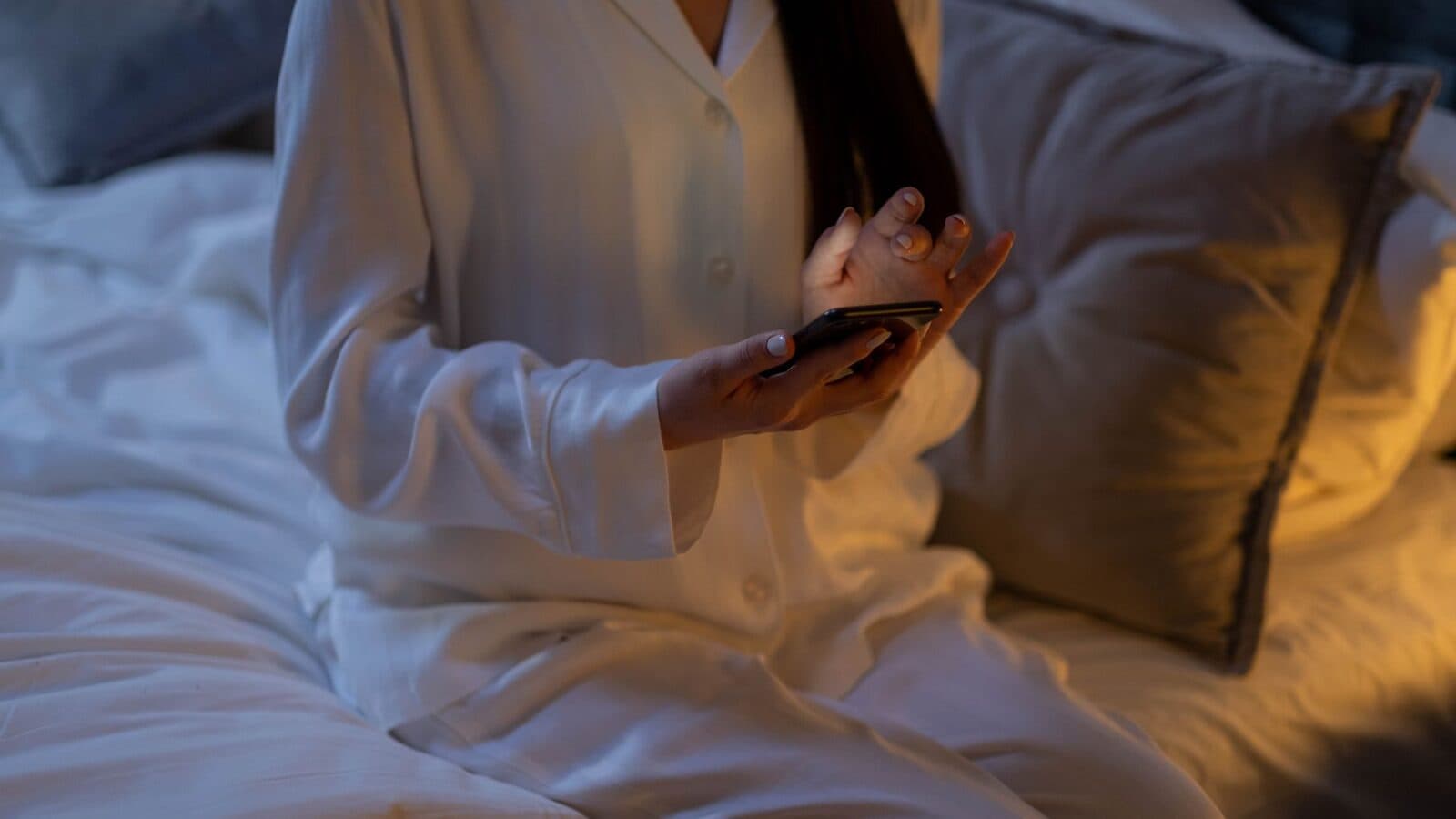 Vrouw in pyjama kijkt in bed op haar telefoon