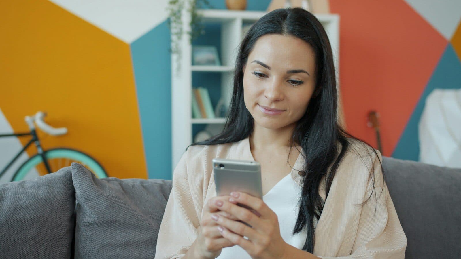 Vrouw op de bank kijkt glimlachend naar haar smartphone