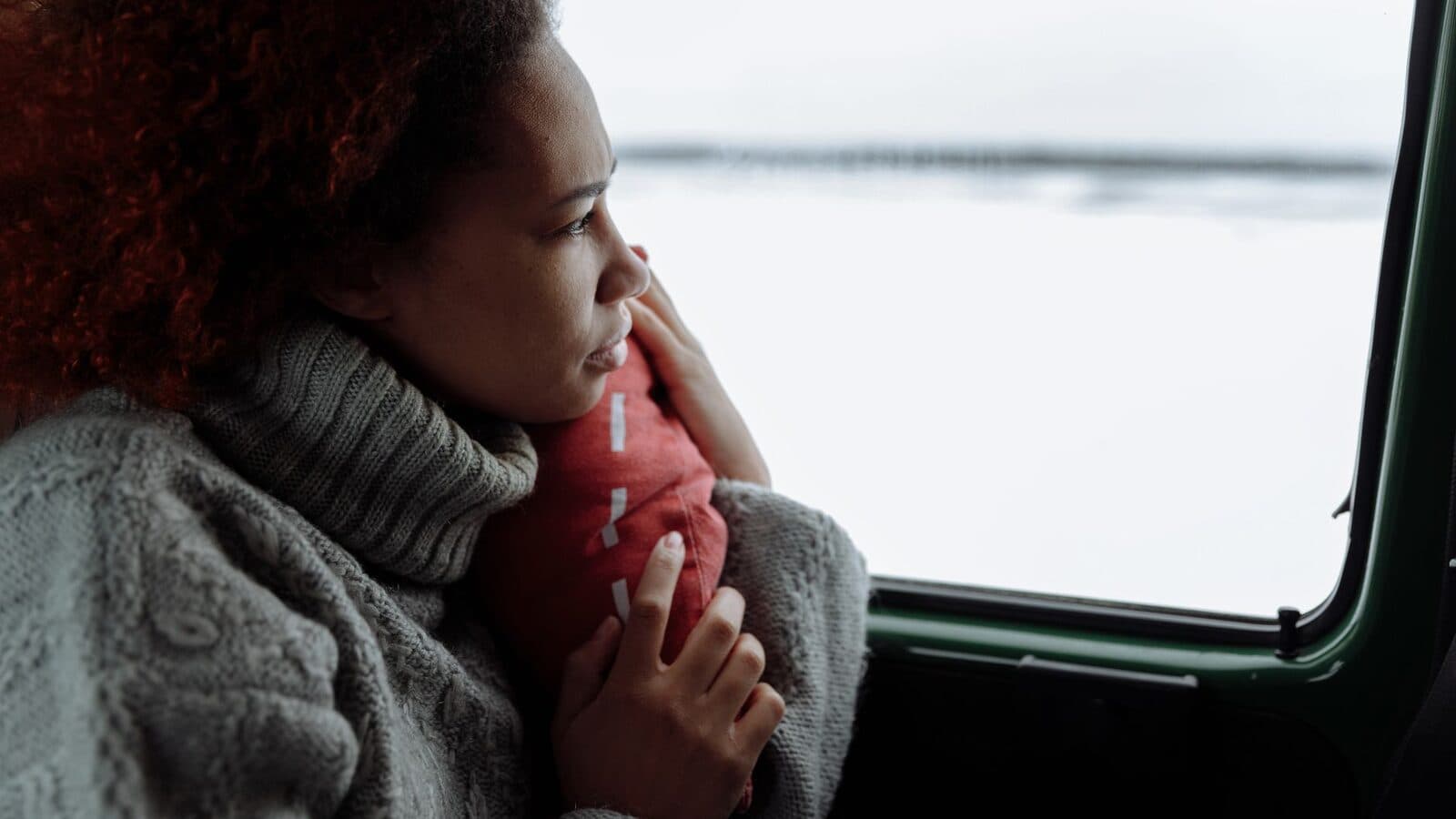 Vrouw in een dikke trui kijkt uit het raam naar een winters landschap