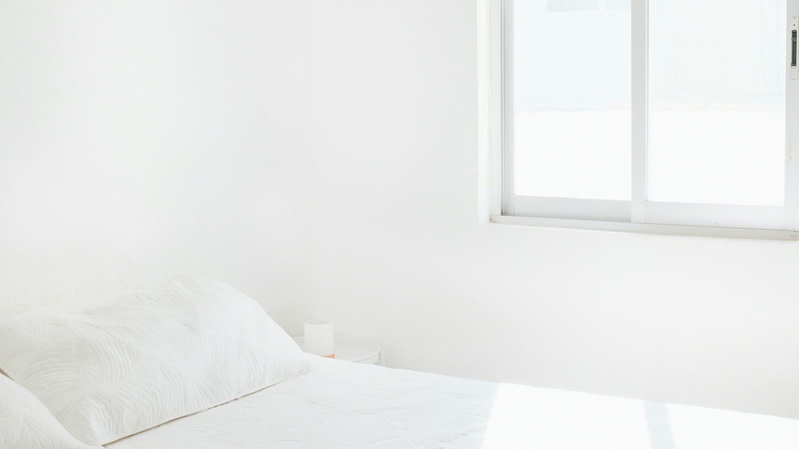Strak opgemaakt wit bed in een lichte slaapkamer