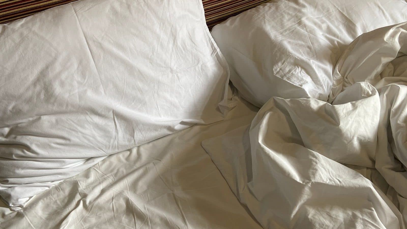 Verkreukeld wit beddengoed op een bed — slaaphygiëne begint bij een rustig bed