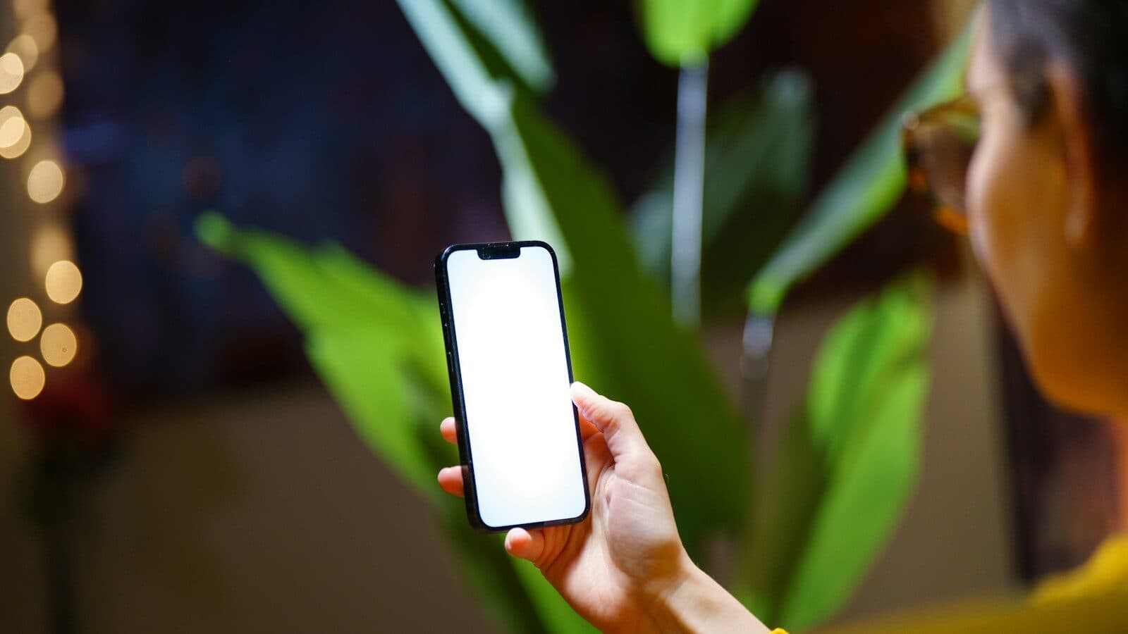 Persoon houdt een smartphone met leeg wit scherm vast, op de achtergrond groene kamerplanten