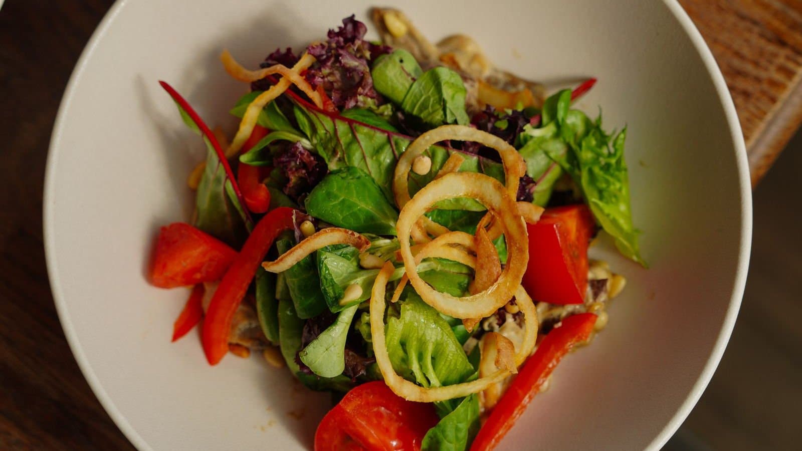 Saladekom van boven met sla, paprika en tomaat — een bord levert meerdere voedingsstoffen tegelijk