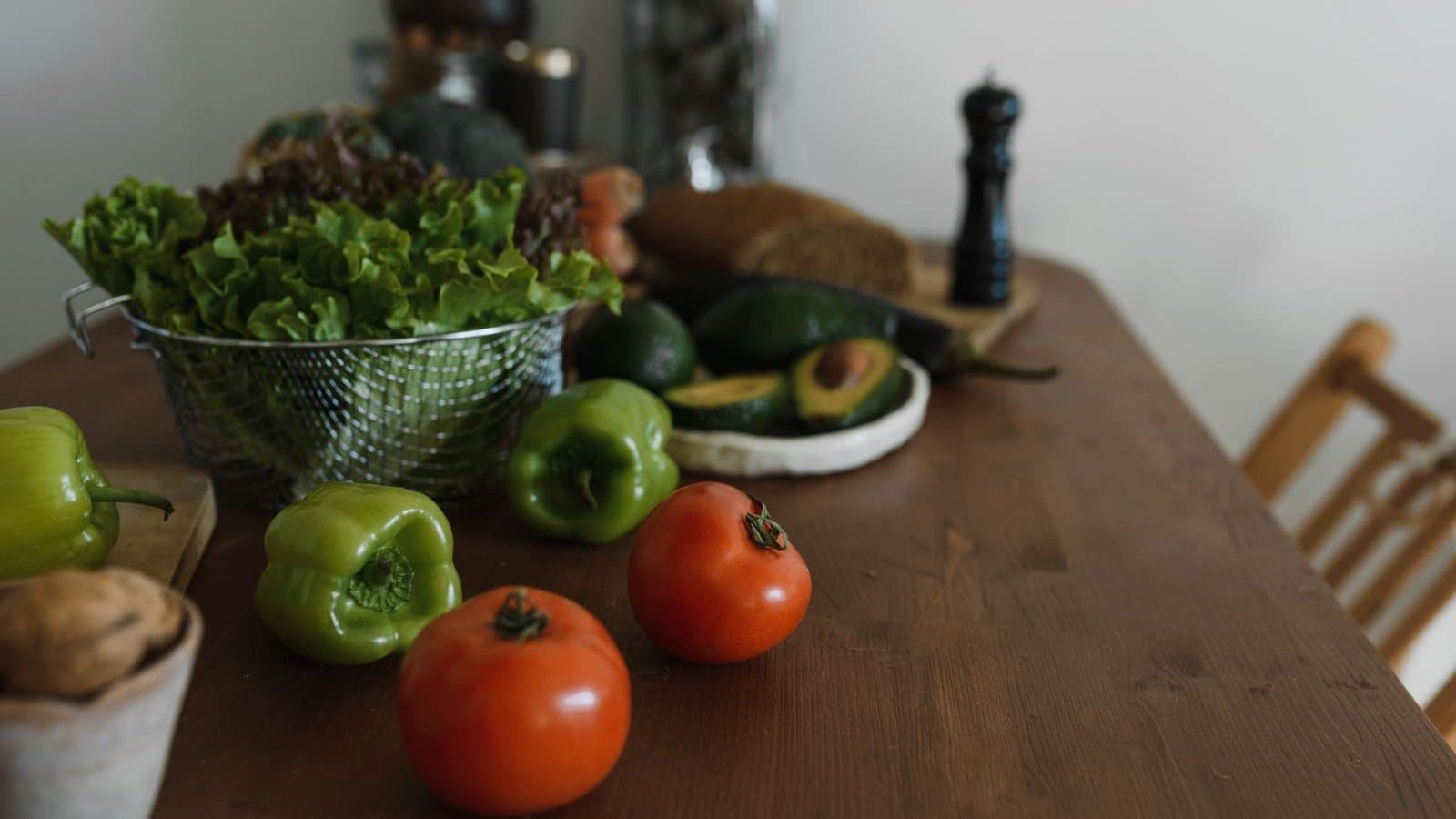 Houten keukentafel met sla, paprika, tomaten en avocado in zacht daglicht — wat je al binnenkrijgt bepaalt je uitgangsstatus